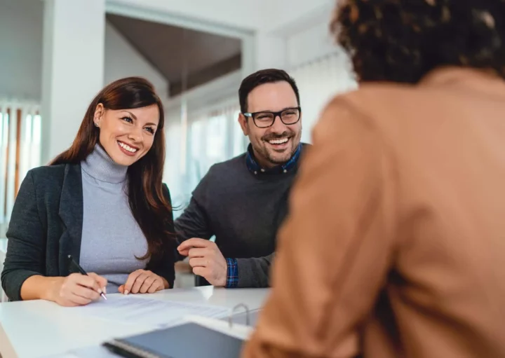 Imagem de um casal formado por um homem e uma mulher no escritório de uma corretora imobiliária assinando um contrato de aluguel